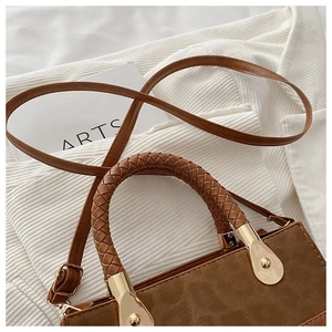 Close-up of brown suede crossbody bag with woven handle and gold-tone metal hardware