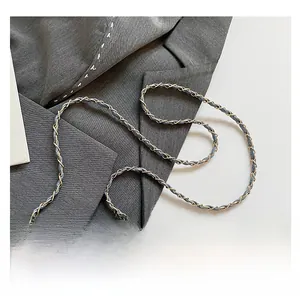 Detail of light blue crossbody bag featuring a golden metal and fabric woven chain strap