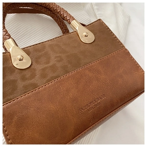 Close-up of brown patchwork handbag featuring woven handle and gold metal hardware