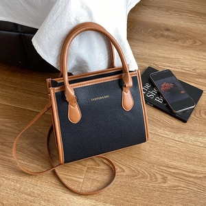 Minimalist black and brown contrast shoulder bag on wooden floor with casual accessories