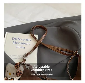 Detail of brown leather tote with adjustable strap and decorative metal chain accent
