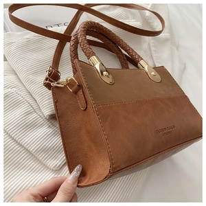 Close-up of brown faux leather bag featuring a chunky braided handle and gold metal hardware