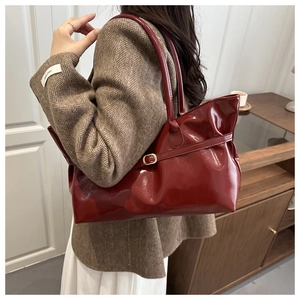 Detail of red patent leather tote bag with gold buckle strap worn with a brown blazer