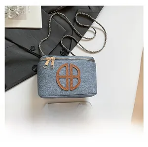 Detailed view of blue denim camera bag with gold chain strap and brown leather logo
