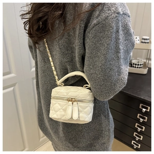 Close-up of a white quilted vanity case bag with gold chain strap worn as a crossbody