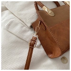 Detail of a brown patchwork crossbody bag with woven handles and golden hardware