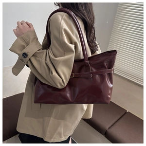 Detail of burgundy glossy tote bag with decorative buckle on a trench coat model