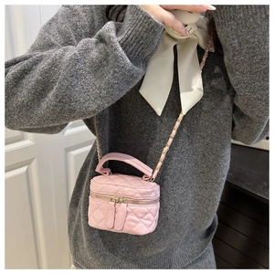 Detail of pink quilted mini bucket bag with gold chain strap and top handle worn by model