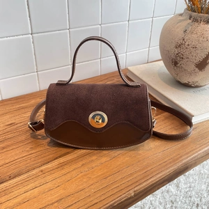 Vintage brown leather semi-circle handbag with gold lock on wooden desk and tile background