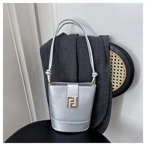 Detailed close-up of a silver bucket bag featuring golden geometric hardware on a black seat