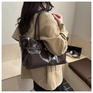 Deep brown glossy tote bag with buckle straps shown in a minimalist office setting