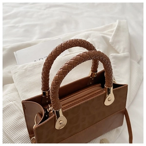 Detail of a brown textured crossbody bag with woven handle and gold hardware components