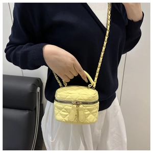 Detail of a yellow quilted mini bag with gold chain strap and top handle held by a model