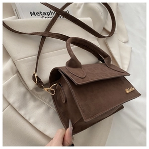 Détail d'un sac bandoulière marron foncé mat avec logo doré sur un tissu de costume beige
