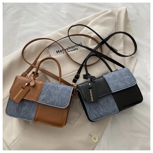 Detail of color-block leather and denim crossbody bag with gold fashion tag on blazer