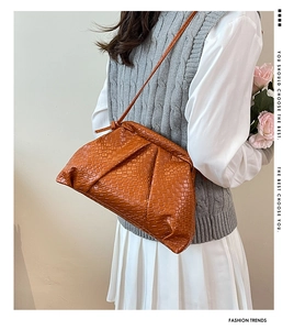 Close-up of orange woven leather shell bag with pleated texture and thin shoulder strap