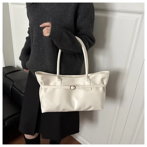 Close-up of cream glossy tote bag with gold buckle and smooth patent leather finish