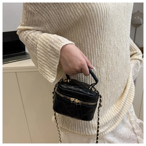 Detail of a black quilted leather mini handbag with gold chain strap and dual zippers