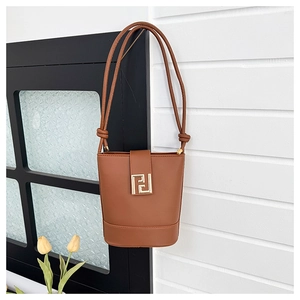 Close-up of caramel leather bucket bag with gold geometric metal buckle on a wall