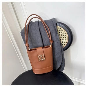 Detail of brown leather bucket bag with gold geometric metal clasp on a textured chair