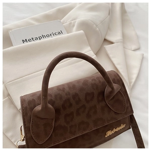 Détail d'un sac à bandoulière léopard marron foncé avec logo doré sur blazer beige