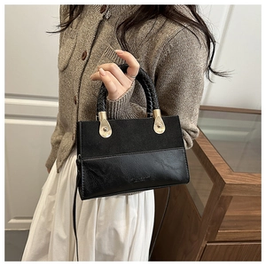 Detail of black crossbody bag featuring matte leather patchwork and woven handle