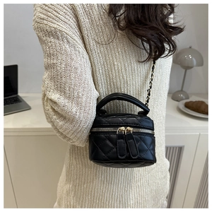 Close-up of a quilted black leather mini box bag with gold chain strap in a cozy interior