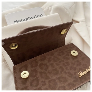 Détail du sac en daim léopard marron foncé avec fermoirs magnétiques dorés et logo métal