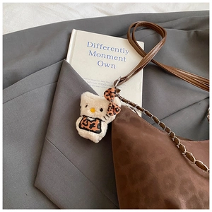 Detail of plush cat charm with leopard bow on a brown suede chain shoulder bag