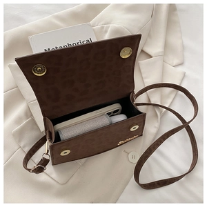 Détail du sac bandoulière léopard vintage avec boucles magnétiques dorées sur costume