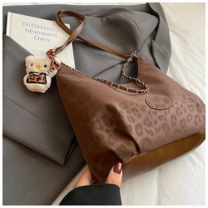 Detailed view of leopard print shoulder bag with brown leather trim and plush charm