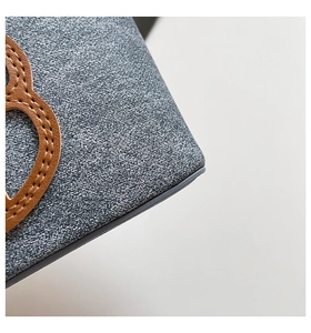 Detail of high-density gray fabric bag featuring a brown leather heart patch and stitching