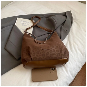 Detail of leopard print shoulder bag with gold chain strap on white fabric surface