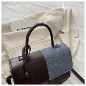 Detail of dual-material crossbody bag with brown leather and blue denim patchwork and gold tag