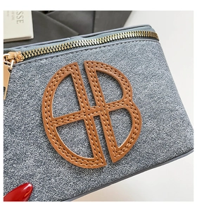 Detail of golden metal zipper and brown leather logo patch on grey denim crossbody bag