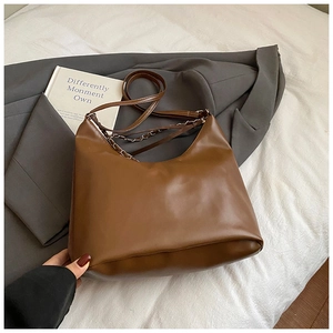 Detailed close-up of brown faux leather shoulder bag with metal chain on fabric