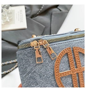 Detail of golden double zipper and brown leather patch on textured light blue handbag