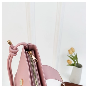 Detail of pink leather handbag showing top zipper closure and unique knotted handle design
