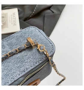 Detail of blue textured fabric bag with golden metal chain strap and zipper close-up