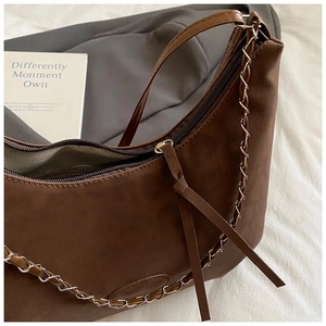 Detail of a brown suede half-moon hobo bag with zipper closure and woven chain strap