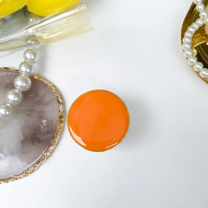 Foldable orange phone grip with gold rim and glossy finish on white marble background
