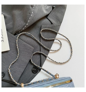 Close-up of light blue denim texture bag with gold chain strap on a grey suit jacket