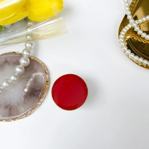 Red folding phone grip with gold metallic edge and glossy finish on marble surface
