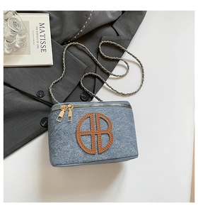 Detailed shot of large denim blue bag with gold chain strap and brown logo patch