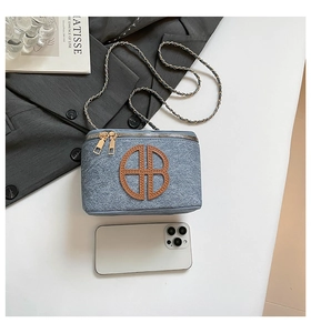 Blue denim crossbody camera bag with leather B logo shown next to a smartphone