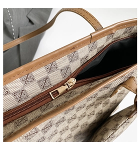 Close-up of canvas tote bag with monogram print and gold zipper detail in brown finish