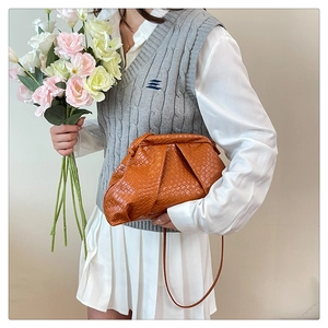 Detail of orange-brown woven cloud clutch bag worn with a casual vest and shirt