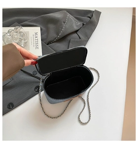 Detail of blue denim crossbody bag with open zipper showing black lining and chain