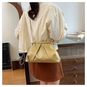 Detail of gold woven shell bag with pleated texture and thin strap held by a model