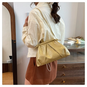 Detail of golden pleated shell bag with crocodile texture worn by a model in a cozy room